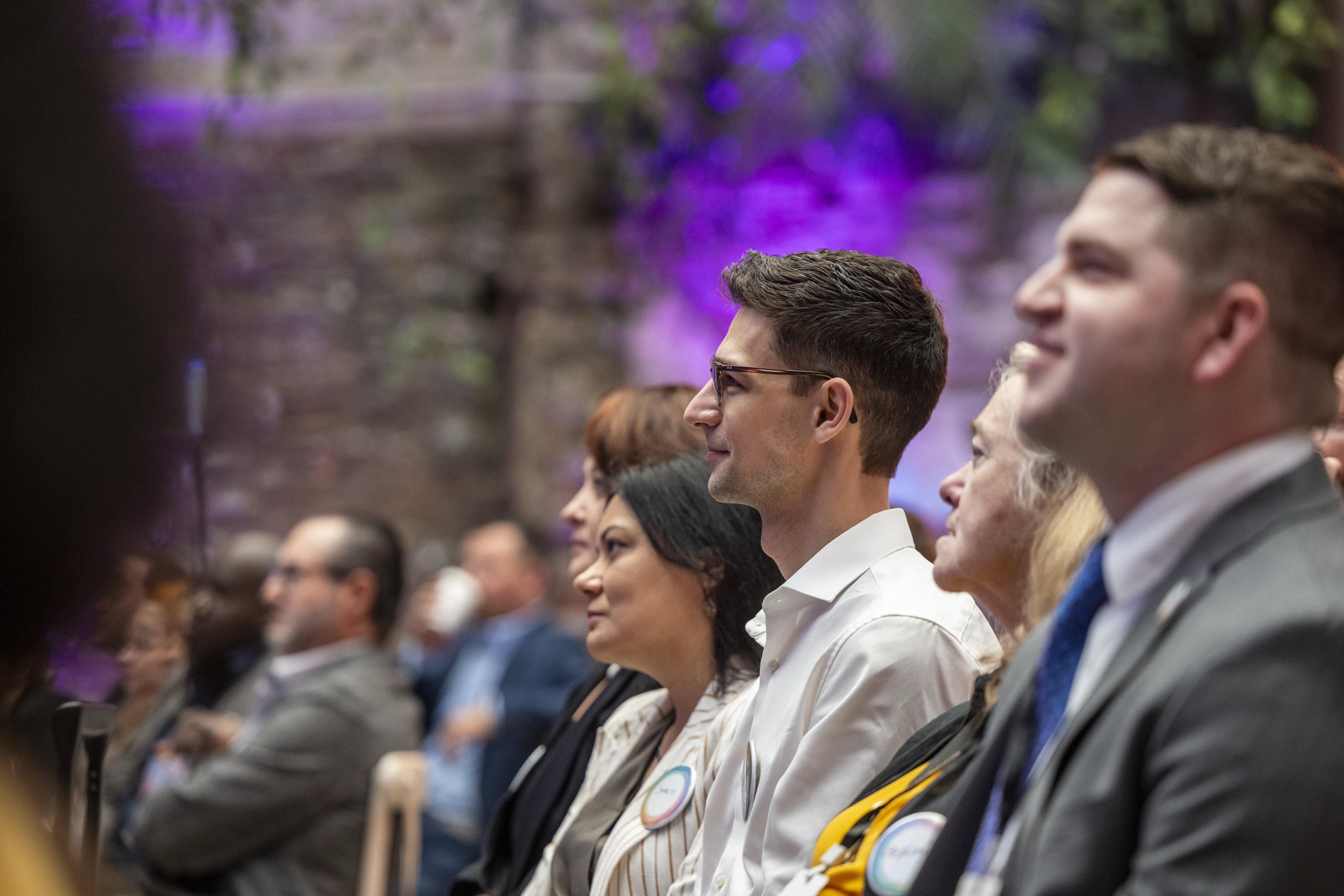 Audience members seated in a row watching a presentation at an Interledger event.